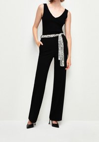 Haut noir sans manches associé à un pantalon noir à jambes larges, rehaussé d'une ceinture blanche et noire à motif. Des talons noirs pointus complètent la tenue.