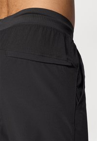 Black athletic shorts with a ribbed elastic waistband and side pocket, made from smooth, lightweight material for comfort and mobility.