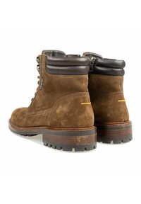 Bruine leren enkellaarsjes van suede met gevoerde donkerbruine leren kraag, een ritssluiting aan de zijkant, robuuste rubberen zolen en houten gestapelde hakken, weergegeven vanuit de achterkant.