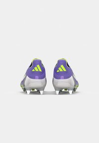 Scarpe da calcio viola e bianche con dettagli gialli, caratterizzate da un design elegante, superiore testurizzato e tacchetti per terreni duri.
