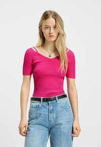 Tajmad rosa ribbad topp med kort ärm, med axelutskärningar och V-ringning, kombinerad med ljusblå högmidjade jeans.