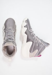 Szare buty sportowe z siateczkowej górnej części, z wyściełanym kołnierzem i białą gumową podeszwą z wzorem w zygzak. Zawierają różowy akcent na pięcie.