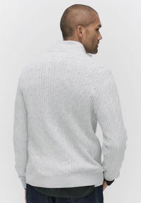 Ljusgrå kabelstickad tröja med ribbat krage och nederkant, med strukturerade mönster och långa ärmar. Baksidan visar en avslappnad passform.