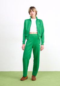 Green tracksuit made of smooth fabric, featuring a zip-up jacket and elastic waistband pants, detailed with white side stripes and Puma logo.