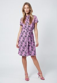 Abito floreale rosa con maniche corte, motivo a foglie nere e vita cinchata. Accompagnato da tacchi a strappo rosa coordinati.