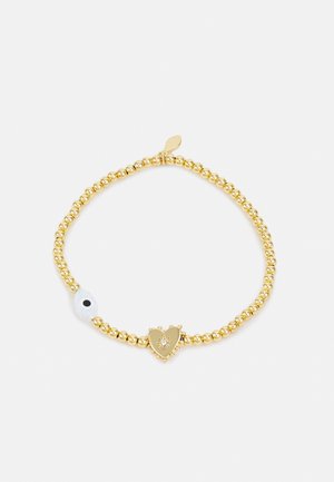 Kultapallero rannekoru, jossa sydämenmuotoinen riipus, jossa pieni kirkas kivi ja valkoinen helmi, jossa musta piste.