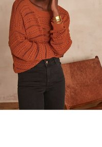 Rostfärgad stickad tröja med öppen väv, rund halsringning och ribbade ärmslut, kombinerad med högmidjade svarta jeans.