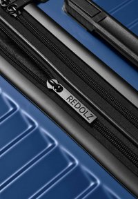 Blauwe harde koffer met zwarte rits en trekhaak met het label "REDOLZ," voorzien van textuur met horizontale ribbels en een zwarte handgreep.