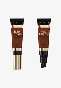 Two tubes of Too Faced Born This Way Soft Matte foundation, featuring a dark brown color, gold accents, and various applicator nozzles.