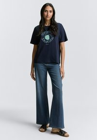 Tamsiai mėlyna medvilninė marškinėliai trumpomis rankovėmis su apskritu grafiką šviesiai mėlyna ir žalia. Derinama su plačiomis tamsiomis džinsinėmis kelnėmis ir juodais sandalais.