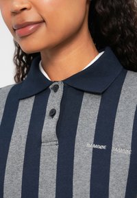 Grå og marineblå stripete polo skjorte med to knapper, kort krage og merke-logo brodert på forsiden. Blandingsmateriale av bomull.