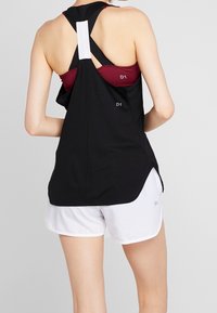 Černý sportovní top s designem na zádech ve tvaru písmene Y, se bílým akcentem a označením "D1." V kombinaci s bílými šortkami.