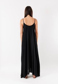 Abito maxi nero con spalline sottili, design fluido e una texture morbida. Presenta una schiena bassa e scende fino alle caviglie.