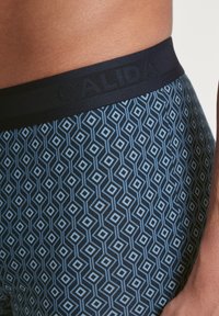 Heren boxershorts met een blauw geometrisch ruitpatroon, marineblauwe tailleband met "CALIDA" branding, gemaakt van soepel, rekbaar materiaal.