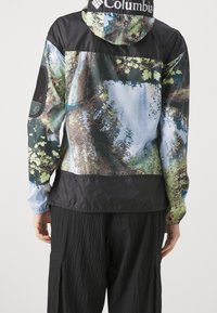 Giacca colorata e decorata con motivo forestale e dettagli neri. Include cappuccio, polsini elastici e tessuto traspirante.