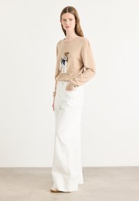 Pulover bej cu un grafic de câine, fabricat dintr-un material moale, asortat cu pantaloni albi cu picioare largi. Are mâneci lungi și guler rotund.