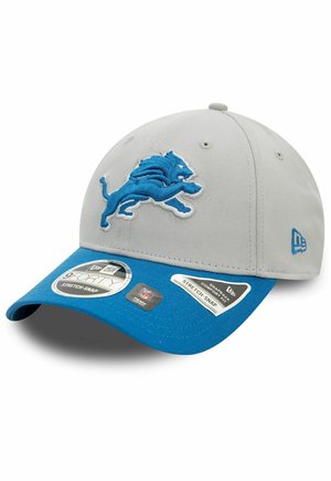 Gorra gris con visera azul, que presenta un logotipo de león azul bordado en la parte frontal. Incluye varias etiquetas en el costado. Diseño de ajuste elástico.