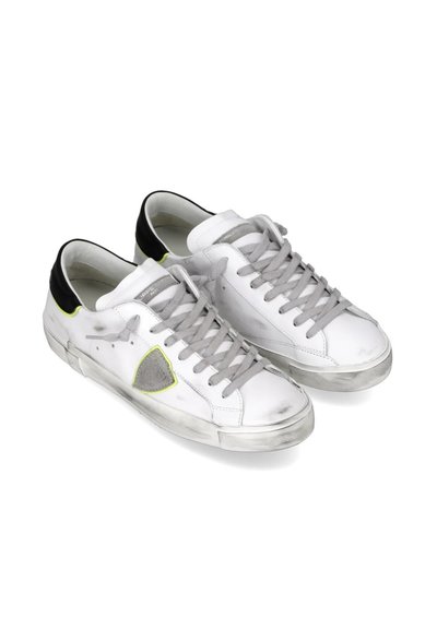 Zapatillas blancas con cordones grises, acentos en el talón negros y un detalle en triángulo verde. Acabado envejecido con una suela de goma texturizada.