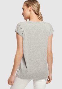 Šedé tričko s krátkým rukávem, ohrnutými manžetami, kulatým výstřihem a volným střihem, vyrobené z měkké látky. Bílé kalhoty viditelné na spodní části.