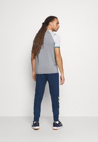 Męski strój sportowy składający się z szarej koszulki z krótkim rękawem i granatowych spodni z zielonymi akcentami. Materiał wydaje się oddychający i gładki.