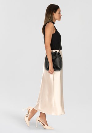 Top senza maniche a coste nere, gonna midi in satin crema, borsa bucket in pelle nera con laccio e scarpe col tacco nudo.