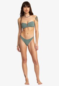 Bikini verde a bandeau con tessuto testurizzato, scollatura a V profonda nella parte superiore e slip bikini a vita bassa coordinati.