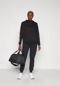 Felpa nera con tasca e coulisse, abbinata a pantaloni jogger neri con dettagli laterali. Sneakers bianche e borsa a tracolla nera.