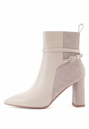 Beige ankelstøvle med spids tå, blokhæl, ruskind og glatte læderpaneler samt en dekorativ rem med metalspænde på siden.