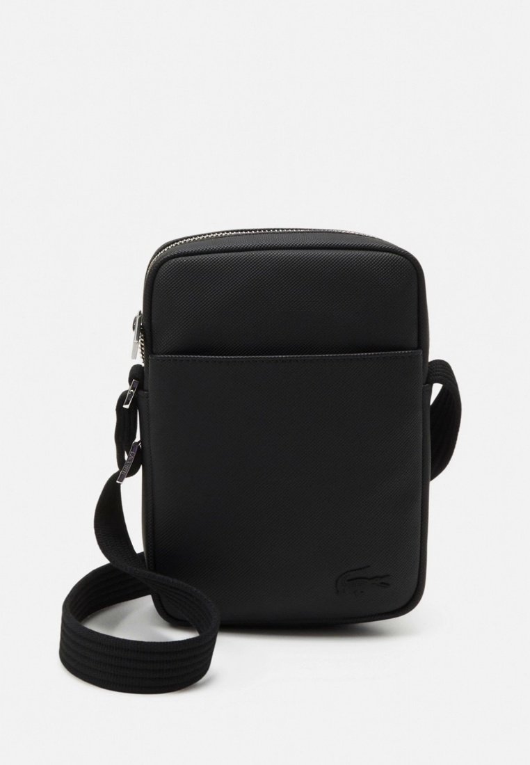Sac bandoulière rectangulaire noir en tissu texturé, avec une poche avant, une fermeture éclair en métal et une sangle réglable.