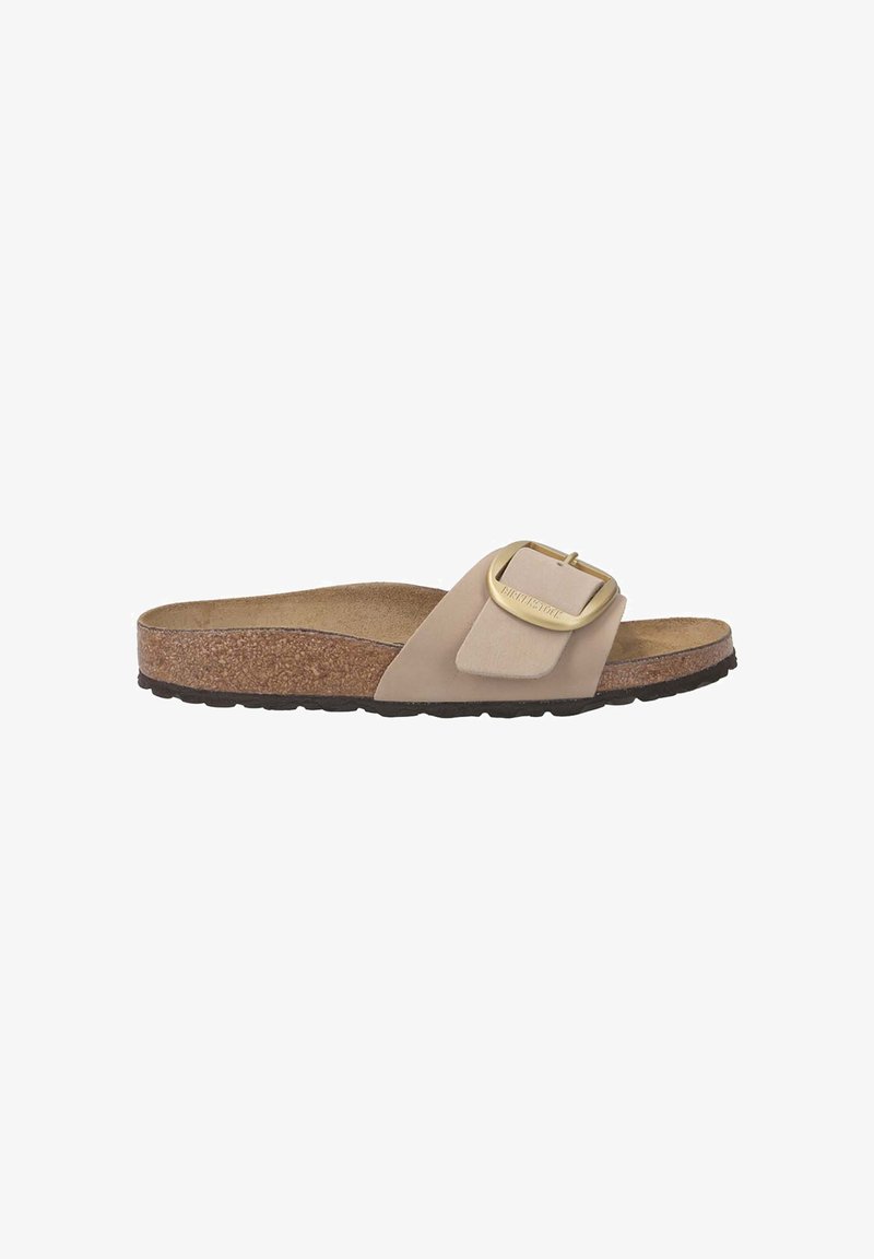 Beige slide sandal with a cork footbed, textured rubber sole, and a large gold-tone buckle accent on a smooth strap.