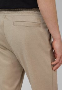 Beige Hosen aus strukturiertem Stoff, mit elastischem Bund und einer Gesäßtasche, die mit einem dezenten Logo-Detail versehen ist.