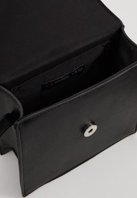 Czarna mini torebka z eko skóry z magnetycznym zatrzaskiem, wyposażona w kontrastowe, czarne wnętrze z tkaniny oraz oznaczoną metką wewnątrz.