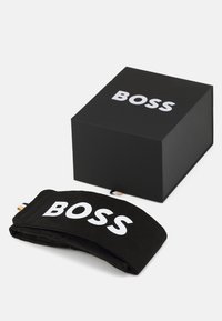 Un bandeau en tissu noir avec le logo "BOSS" en blanc, placé à côté d'une boîte rectangulaire noire arborant le même logo en blanc.