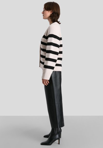 Cardigan a righe in crema e nero, texture a maglia, apertura frontale, abbinato a pantaloni in pelle nera a vita alta e stivaletti con punta.