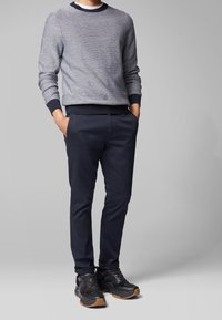 Gråstickad tröja med marinblå muddar, tillsammans med marinblå byxor med subtil textur och svarta sneakers med gummisulor.