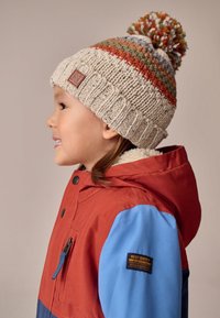 Világosbézs kötött sapka sokszínű csíkokkal, színes pomponnal a tetején. Piros-kék összevágott kabát fekete címkével.