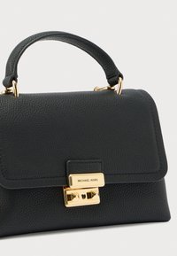Bolso de mano de cuero negro texturizado con asa corta y cierre dorado grabado con "Michael Kors" sobre fondo blanco.