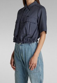 Mörkblå kortärmad skjorta med krage som knäpps, två bröstfickor och cinchad midja. Matchas med lösa ljusblå jeans.