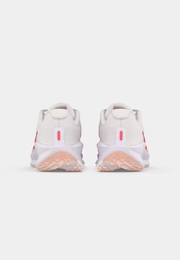 Zapatillas deportivas blancas con acentos rojos, textura de malla, cuello acolchado y suela de goma rosa, que cuentan con una lengüeta en el talón distintiva y un patrón de agarre.