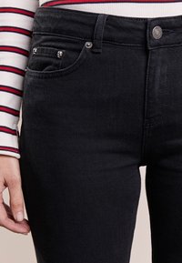 Svarta denimjeans har en smal passform, fem-fickorsdesign och metallknappdetaljer. Tyget har en mjuk struktur med minimal slitage.