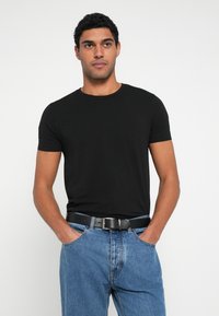 Camiseta de algodón negra con mangas cortas y escote redondo; combinada con vaqueros de mezclilla azul claro y cinturón negro. Diseño sencillo y ajustado.