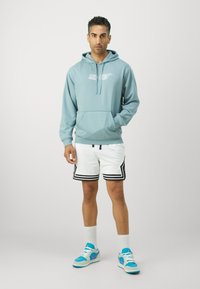 Lysblå pullover hoodie med et centreret hvidt grafik, parret med hvide shorts med sorte kanter og accenter, samt blå sneakers.