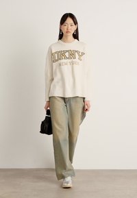 Lys kremfarget strikket genser med "DKNY NEW YORK" i gull. Kombinert med løse, falmede lyseblå bukser og grå sneakers. Tilbehør med en svart veske.