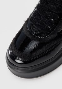 Musthave musta lakknahkist sneaker, millel on pehmea musta karu aksent varvaste juures ja tekstureeritud must kangas keel, millel on ümmargused mustad paelad.