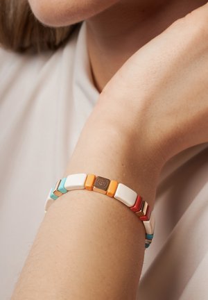 Buntes elastisches Armband mit ineinandergreifenden Teilen in Weiß, Orange, Rot und Türkis, mit einem metallischen Akzent in der Mitte.