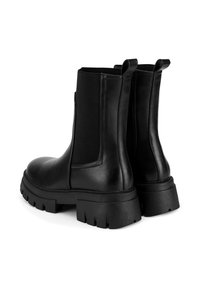 Botines de cuero negro con paneles elásticos en los laterales, suela plataforma gruesa y tiradores para facilitar su uso. Textura lisa con detalles mínimos.