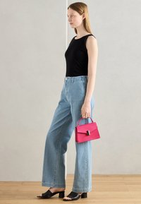 Czarny top bez rękawów, jasnoniebieskie dżinsy o szerokich nogawkach, czarne sandały na szerokim obcasie, trzymająca małą różową torebkę z srebrną klamrą.