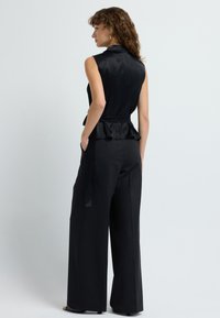 Top negro sin mangas con cintura peplum, combinado con pantalones anchos negros. Tela suave con un brillo sutil. Diseño elegante.
