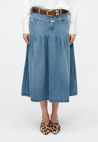 Jupe longue en denim avec un design à étages, de couleur bleu clair, et une ceinture en cuir marron. Elle est dotée de poches et est associée à des chaussures imprimées léopard.