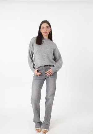 Grijze gebreide trui met een hoge hals en een ontspannen pasvorm, gecombineerd met lichtgrijze rechte jeans en beige open teen sandalen.